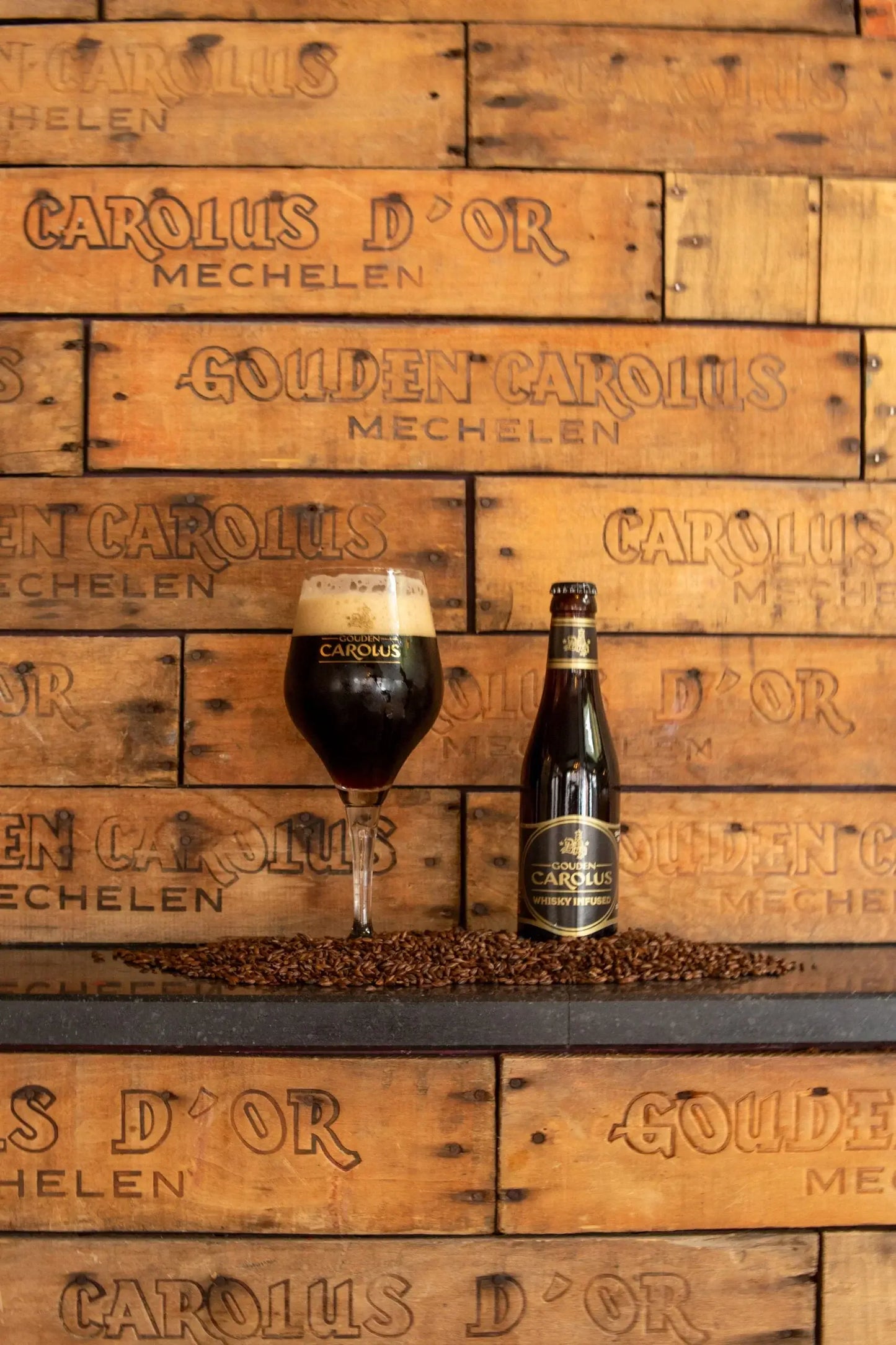 Flasche Gouden Carolus Whisky Infused 33cl mit vollem, schaumigem Bierglas auf braunem Holztisch mit eingraviertem Markenlogo.