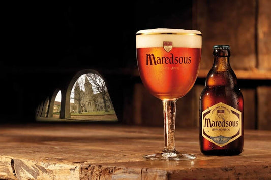Maredsous Abbaye Blond Bierglas mit Schaum und Flasche auf rustikalem Holztisch.