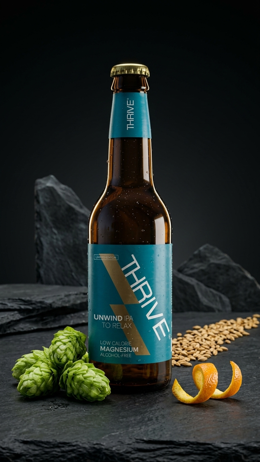 Braune Glasflasche Thrive Peak alkoholfreies IPA mit blauem Etikett, daneben Hopfen und Orangenschale.
