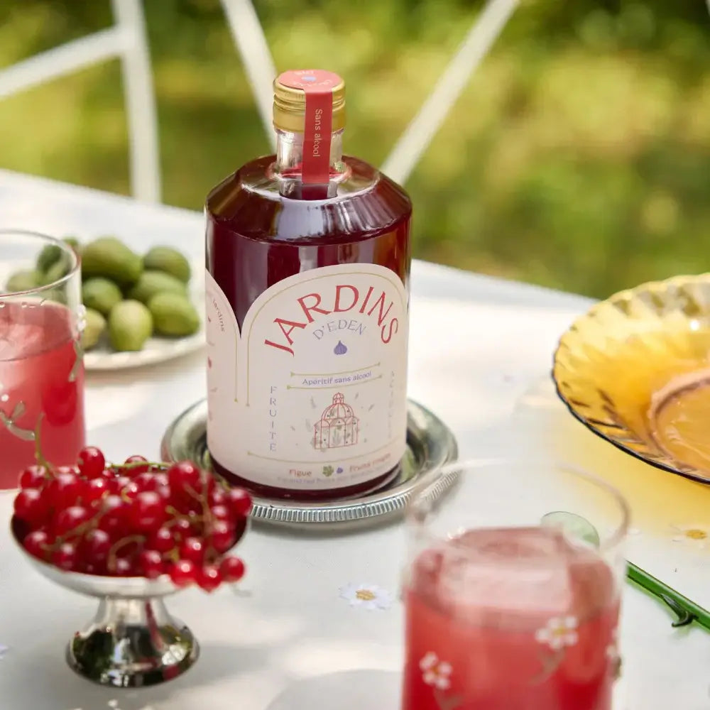 70-cl-Flasche alkoholfreies Getränk „Jardins“ mit rotem Etikett auf weißem Gartentisch, umgeben von roten Beeren und grünen.